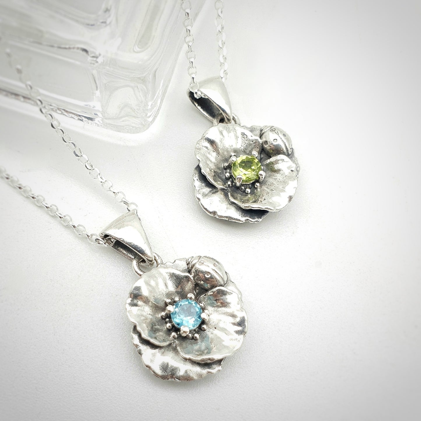 Ciondoli in argento 925 con papavero e coccinella, incastonati al centro un peridoto e un'apatite taglio brillante.