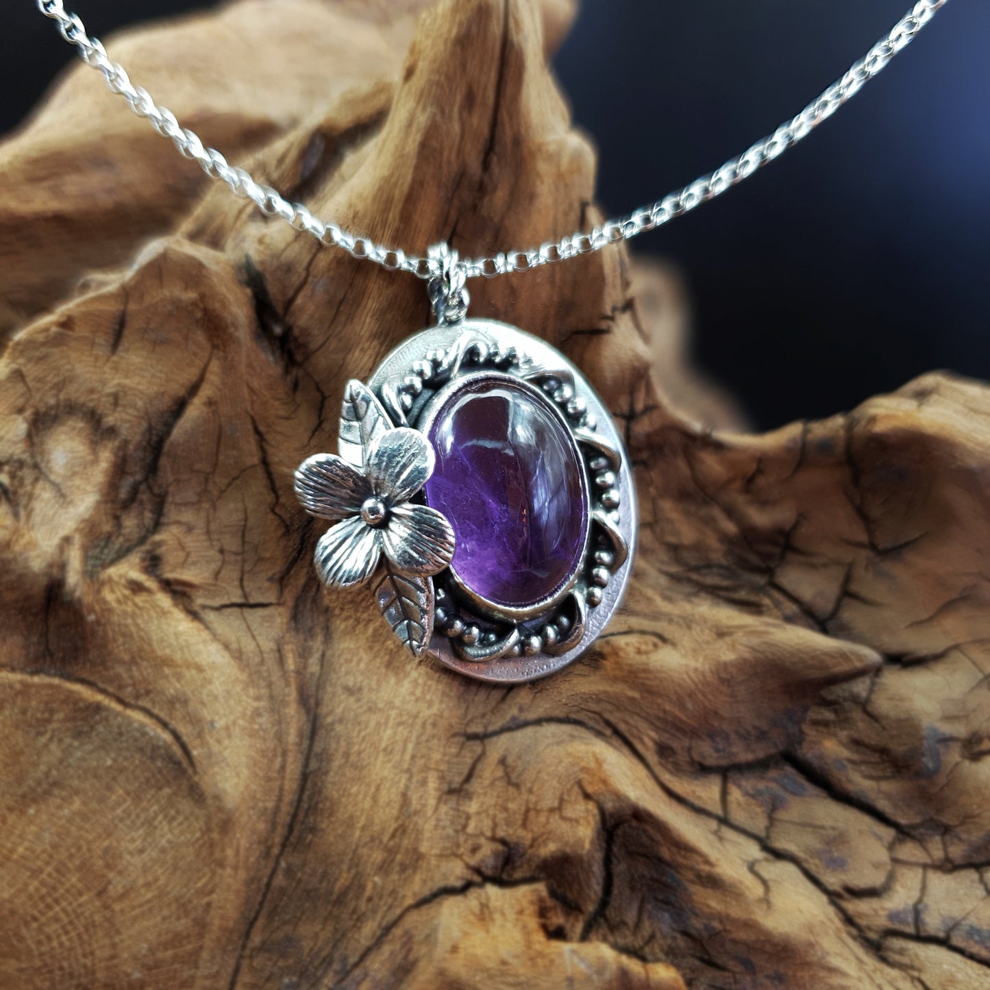 Ciondolo in argento 925 con cabochon di ametista, decorazioni intrecciate di filo, fiore semplice e foglie.