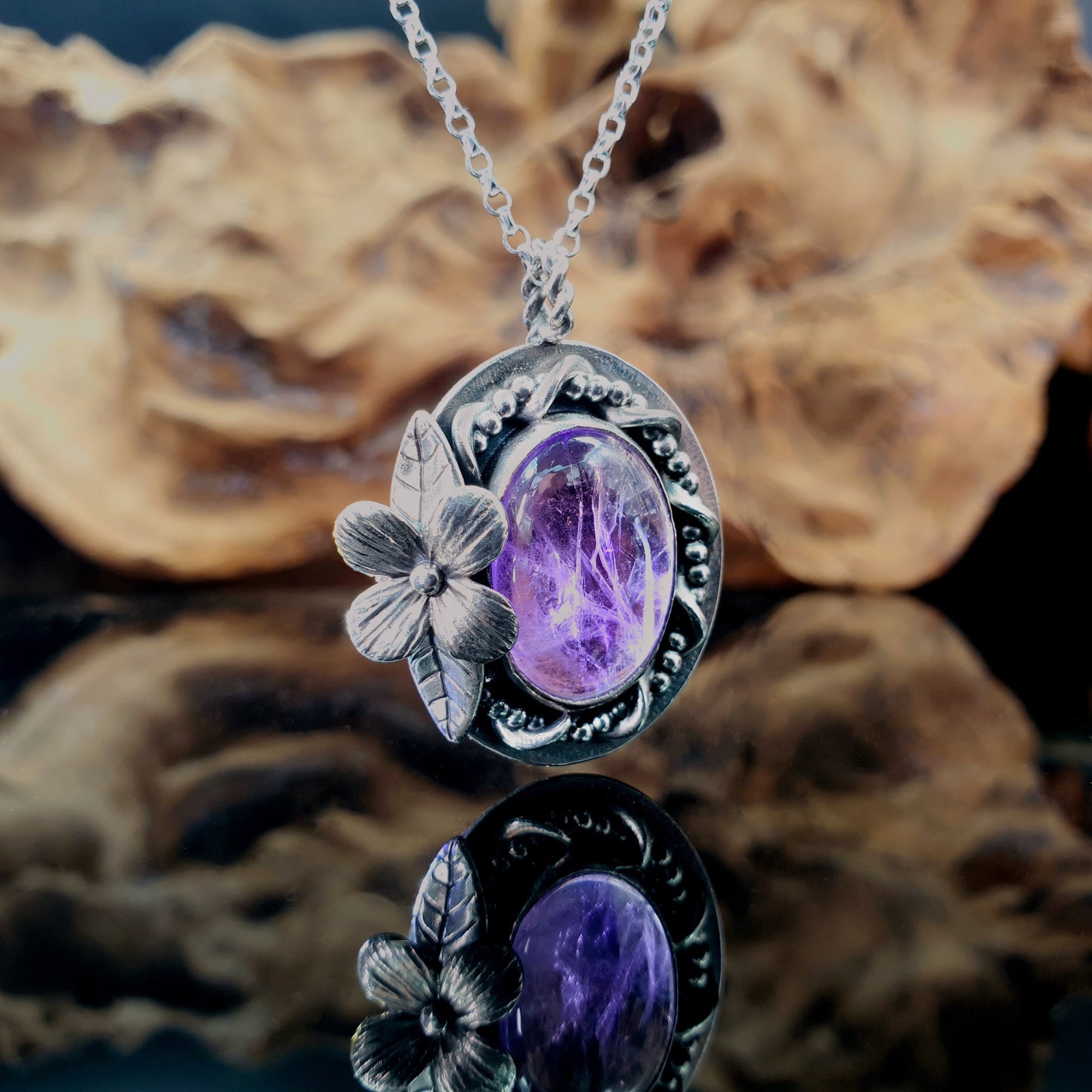 Ciondolo in argento 925 con cabochon di ametista, decorazioni intrecciate di filo, fiore semplice e foglie.