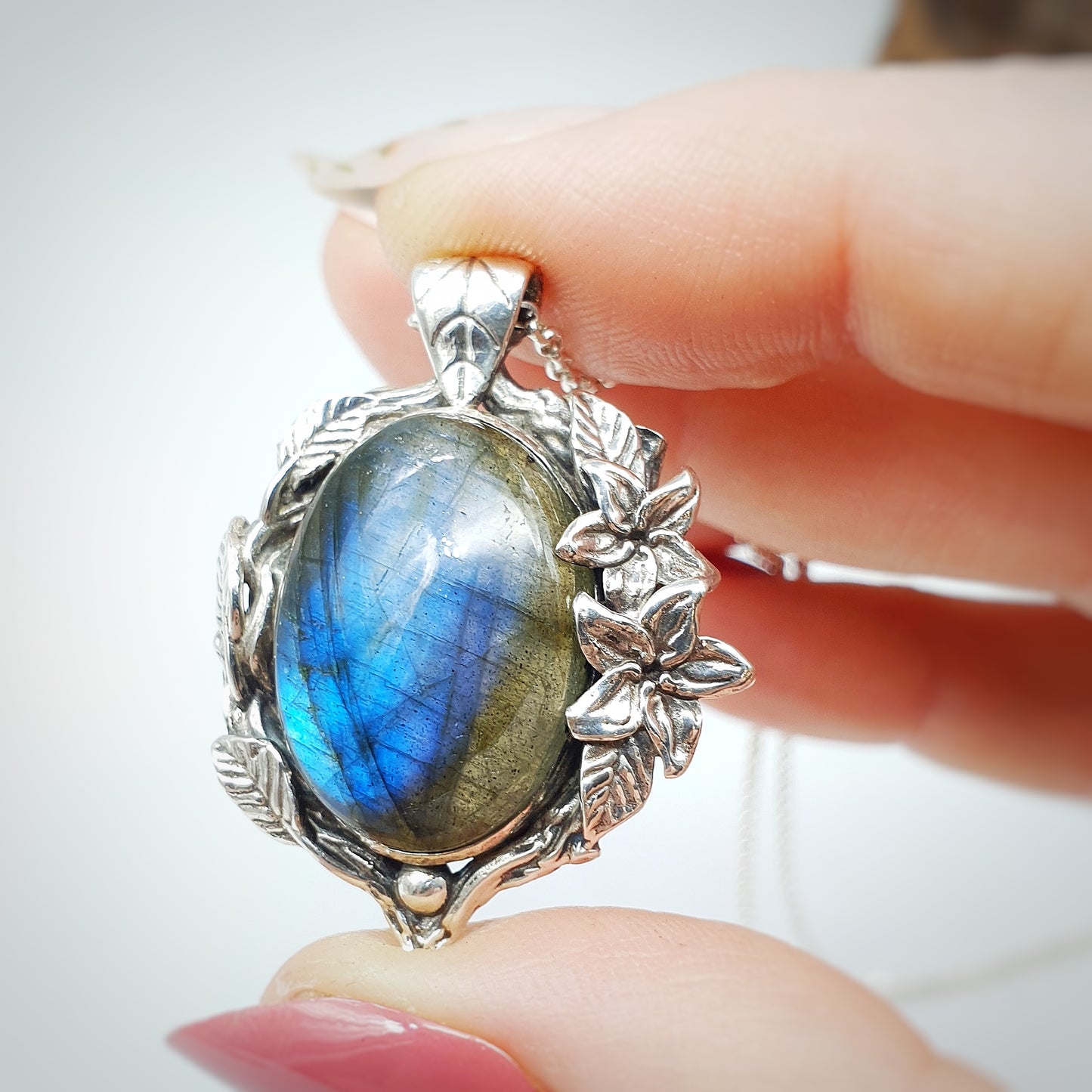 Ciondolo in argento con labradorite multicolor ovale, incorniciata da rametti con foglie e gelsomini notturni.