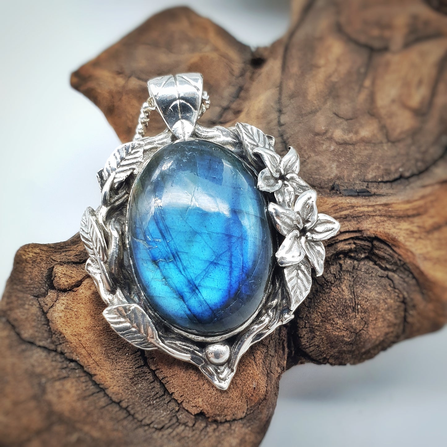 Ciondolo in argento con labradorite multicolor ovale, incorniciata da rametti con foglie e gelsomini notturni.