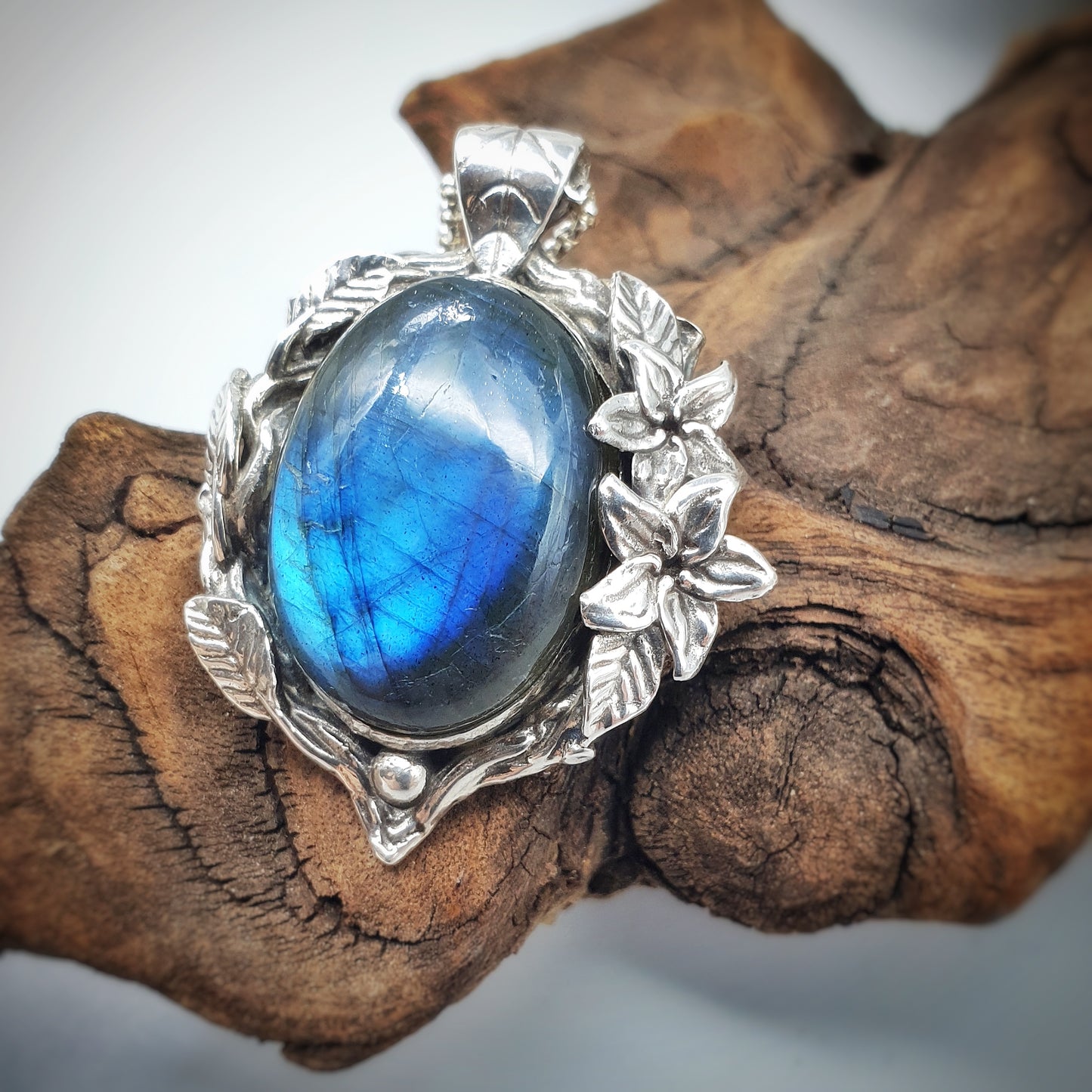 Ciondolo in argento con labradorite multicolor ovale, incorniciata da rametti con foglie e gelsomini notturni.