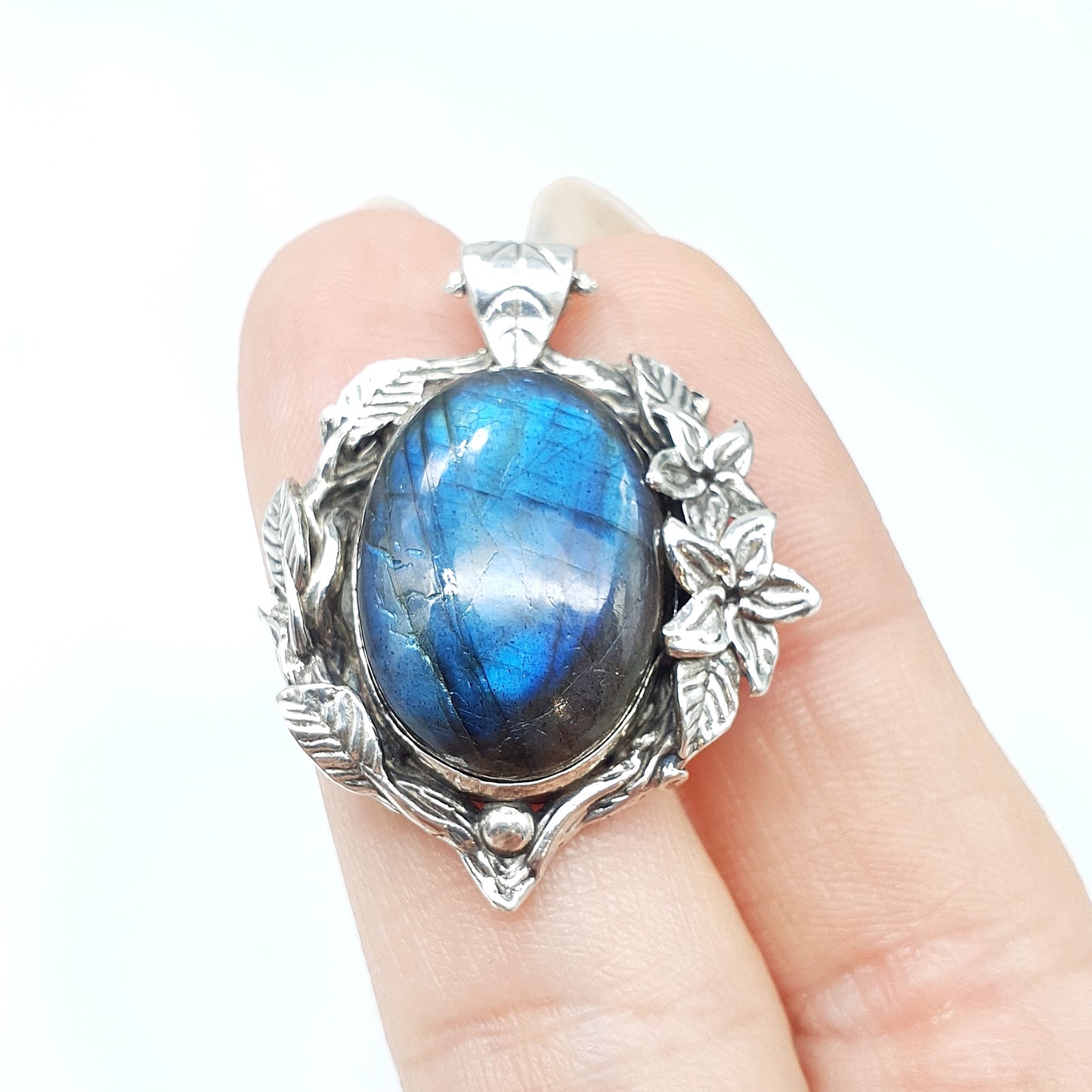 Ciondolo in argento con labradorite multicolor ovale, incorniciata da rametti con foglie e gelsomini notturni.