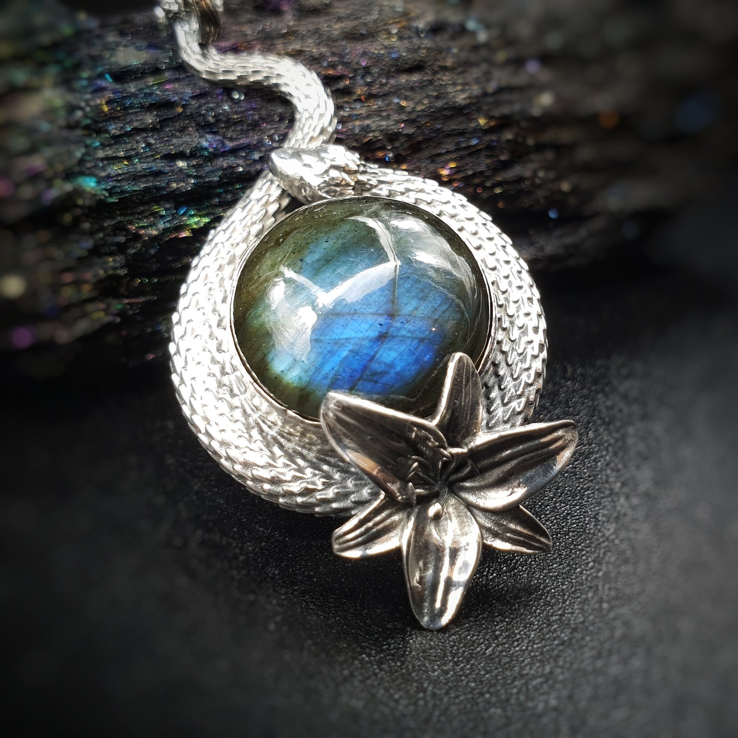 Ciondolo in argento 925 formato da un serpente che avvolge un cabochon di labradorite multicolor, con un giglio nella parte bassa.