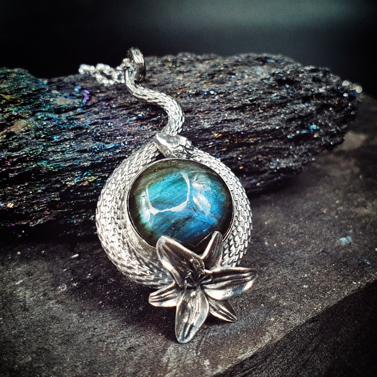 Ciondolo in argento 925 formato da un serpente che avvolge un cabochon di labradorite multicolor, con un giglio nella parte bassa.