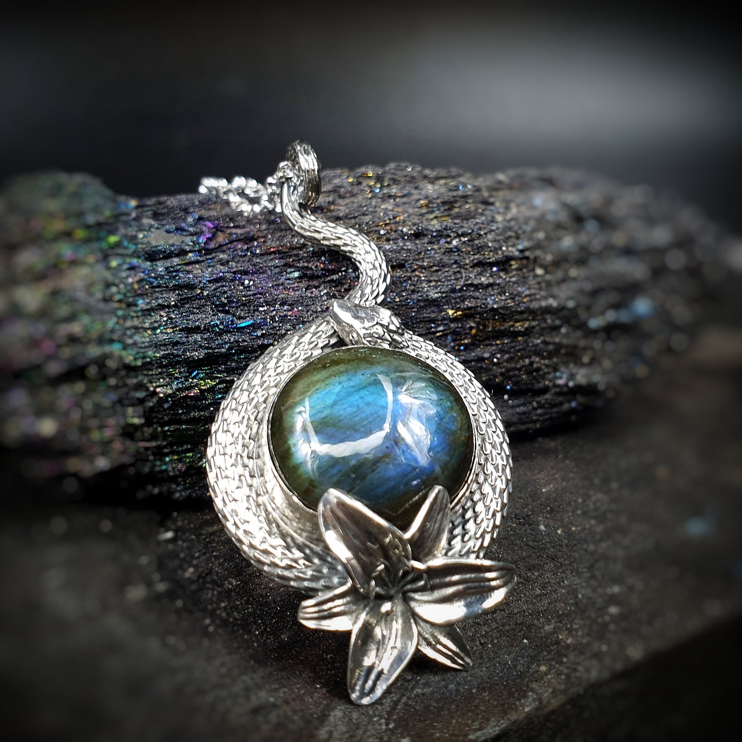 Ciondolo in argento 925 formato da un serpente che avvolge un cabochon di labradorite multicolor, con un giglio nella parte bassa.