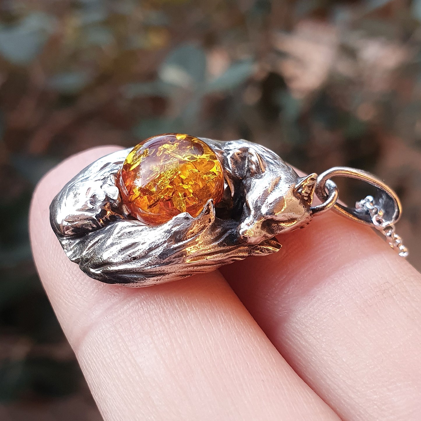 Una micro-scultura in argento 925 raffigurante una volpe acciambellata attorno ad un cabochon di ambra baltica.