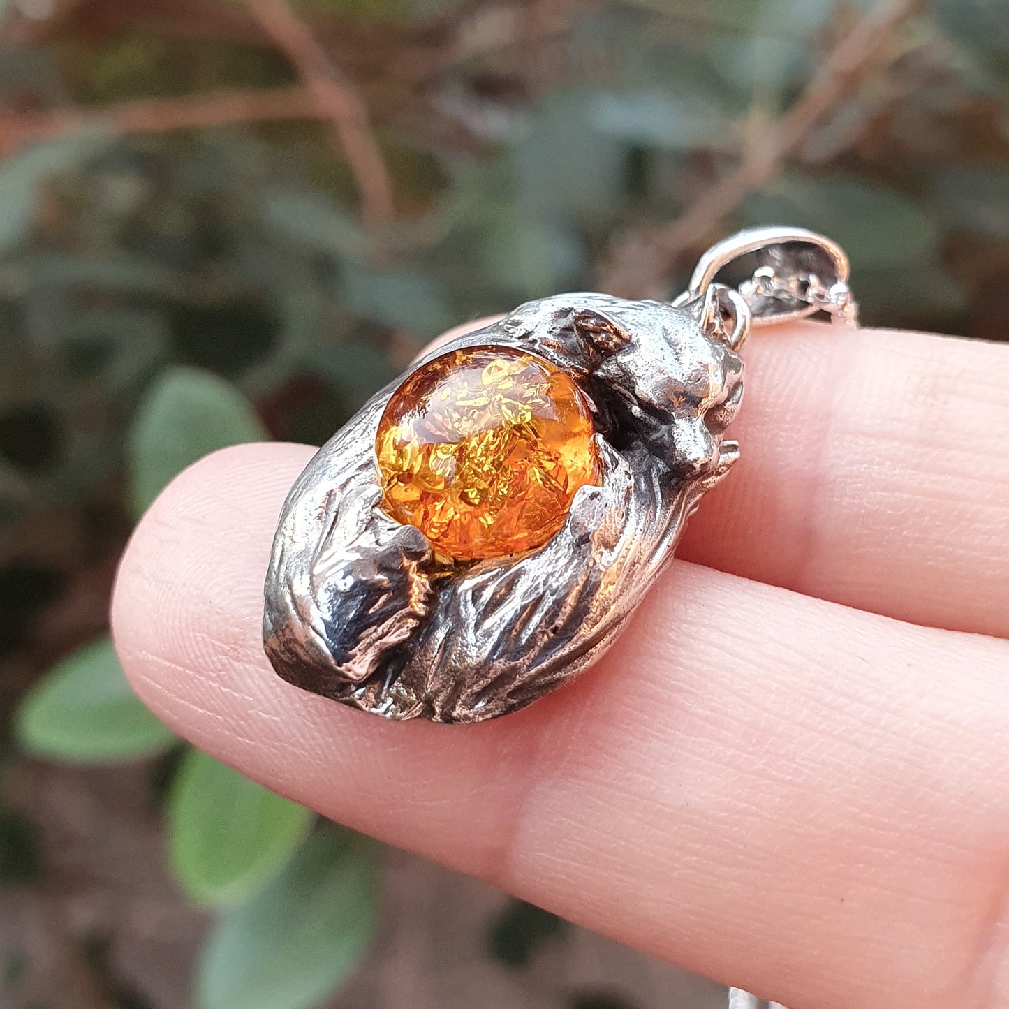 Una micro-scultura in argento 925 raffigurante una volpe acciambellata attorno ad un cabochon di ambra baltica.
