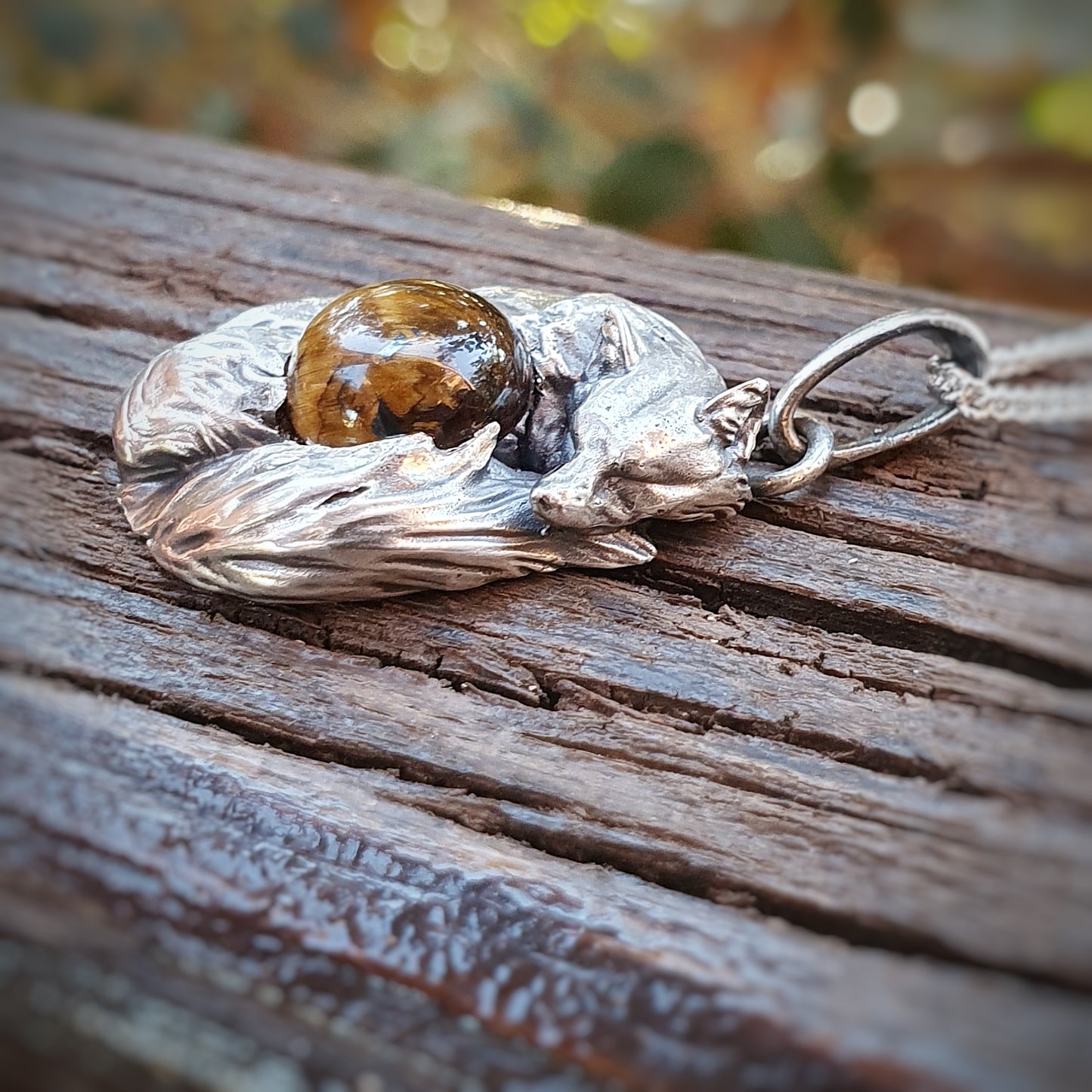 Una micro-scultura in argento 925 raffigurante una volpe acciambellata attorno ad un cabochon di occhio di tigre.