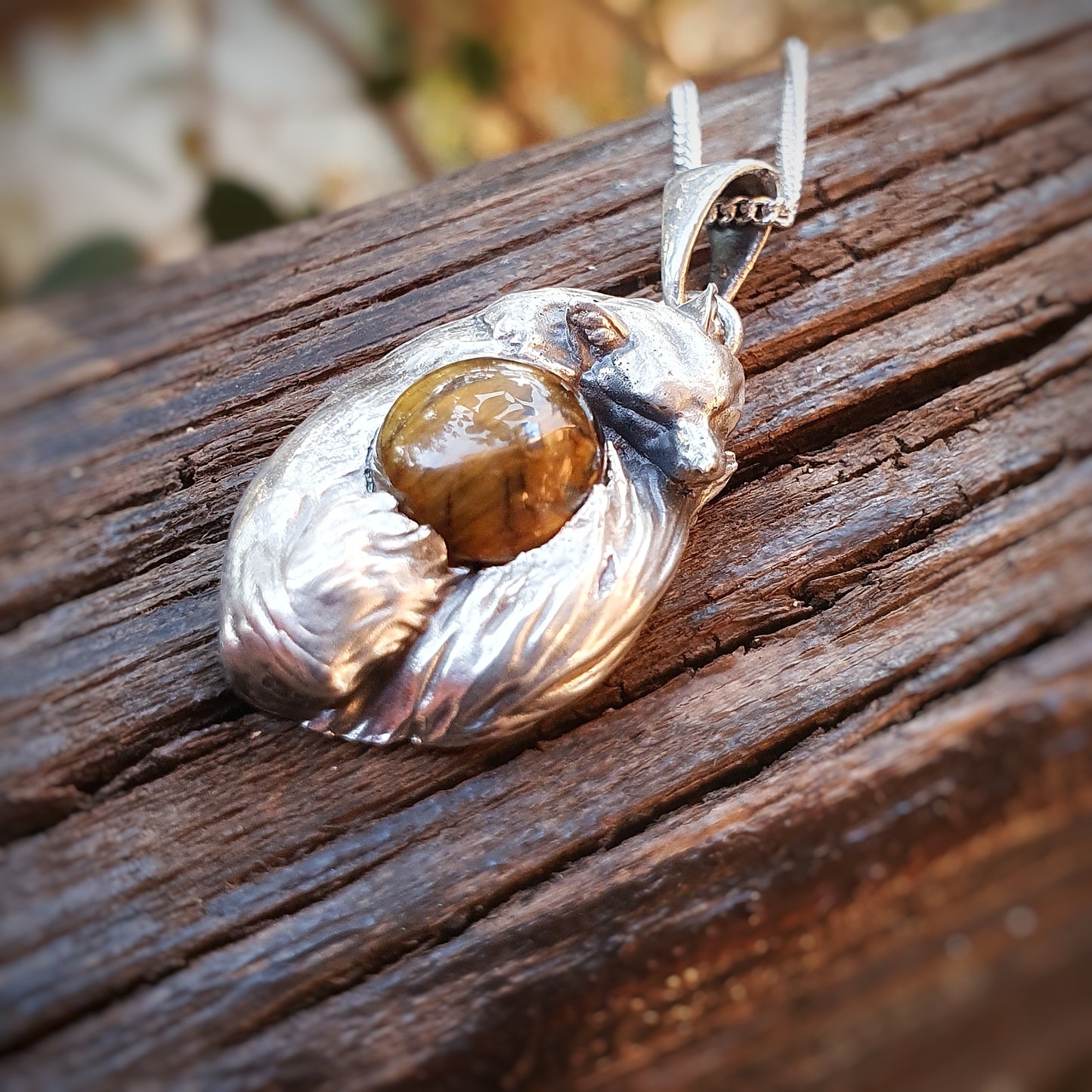 Una micro-scultura in argento 925 raffigurante una volpe acciambellata attorno ad un cabochon di occhio di tigre.