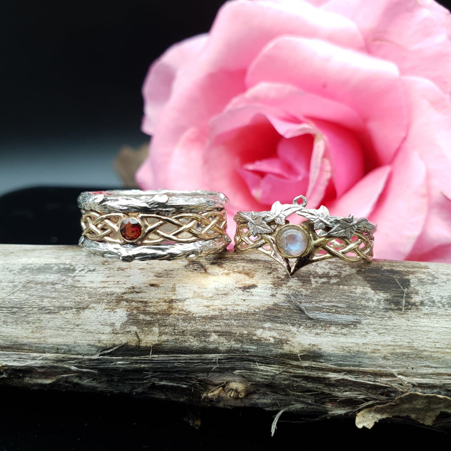 Coppia di fedi in argento e oro 14kt con labradorite e granato, poggiate su legna secca.