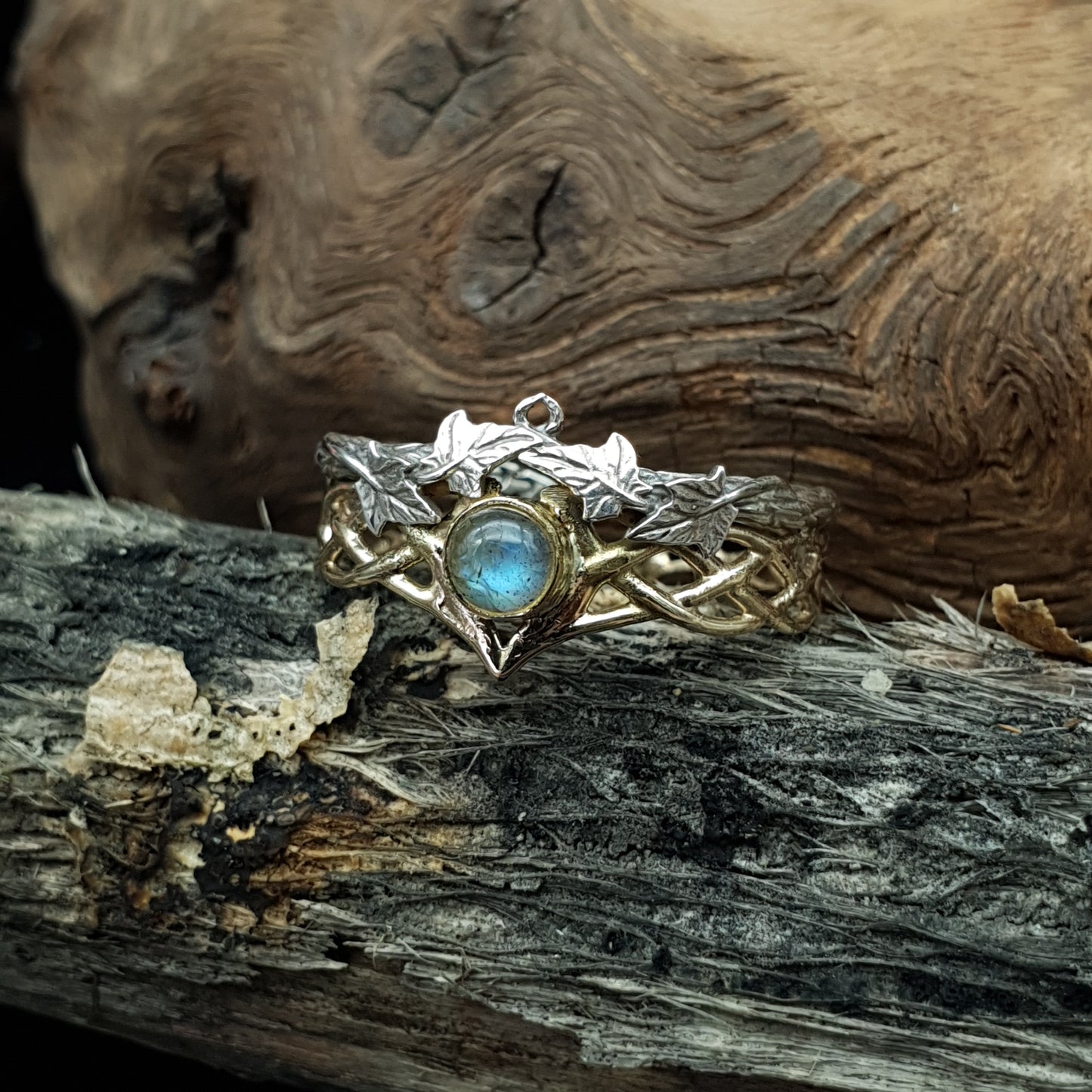 Fede in argento e oro 14kt con labradorite, poggiata su della legna secca.