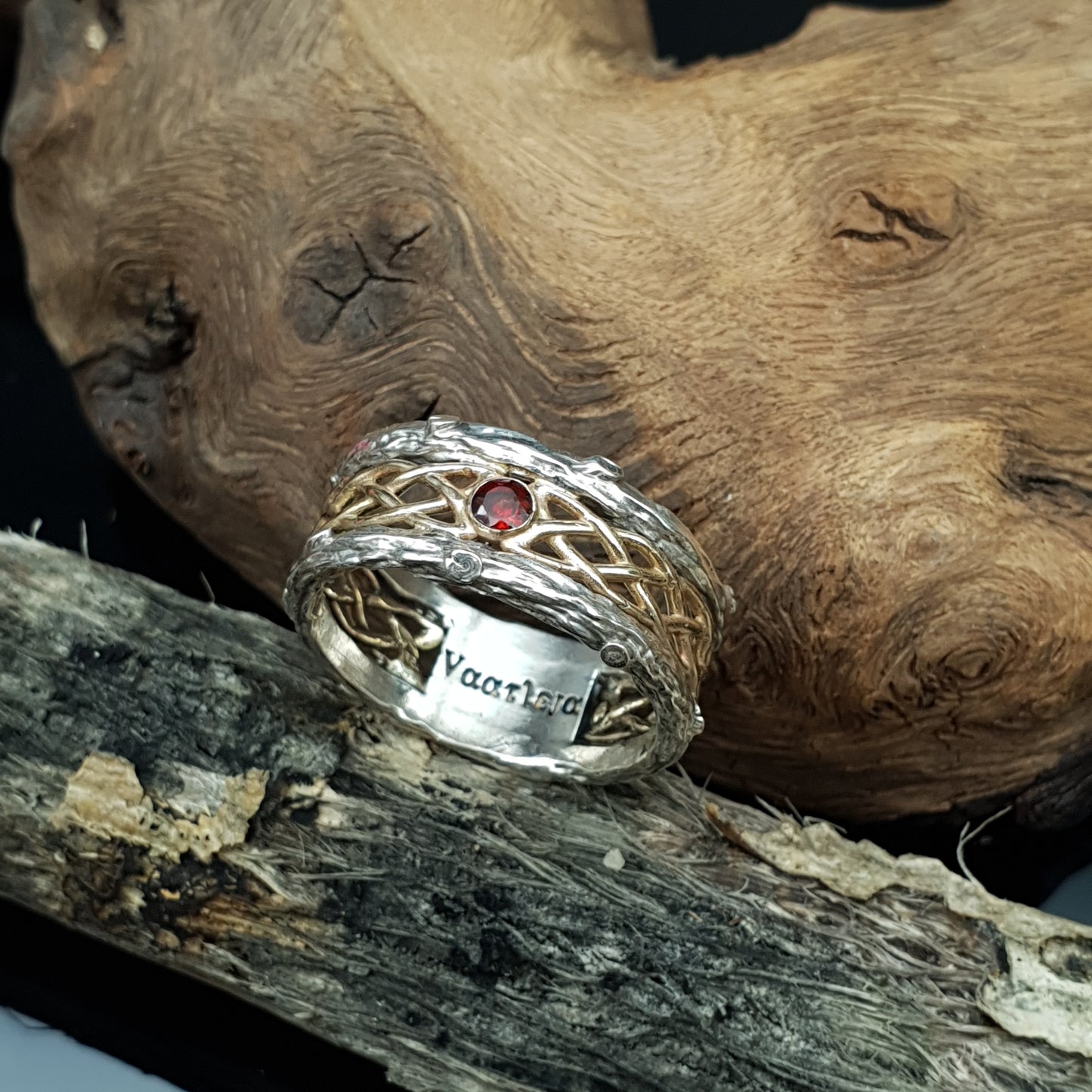 Fede in argento e oro 14kt con granato, poggiata su della legna secca.