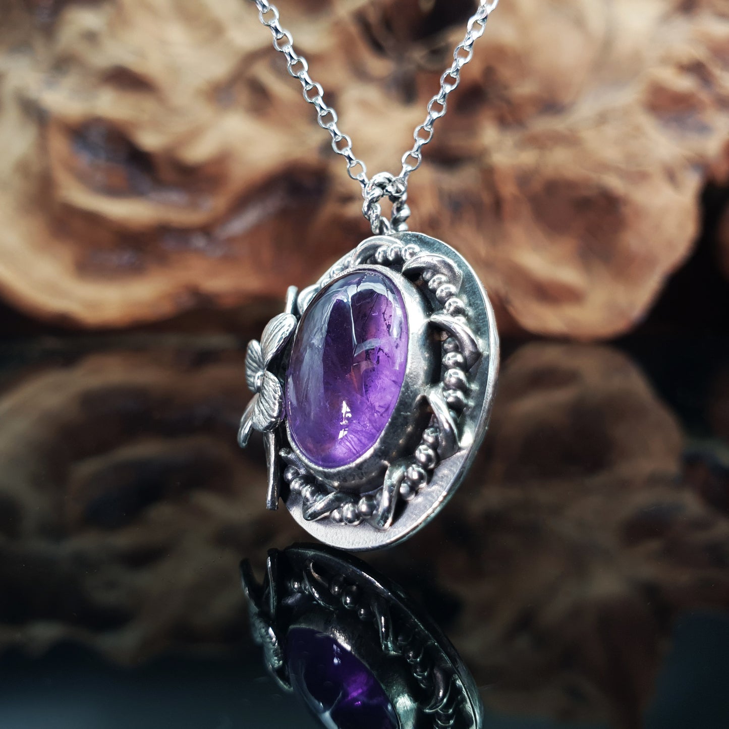 Ciondolo in argento 925 con cabochon di ametista, decorazioni intrecciate di filo, fiore semplice e foglie.