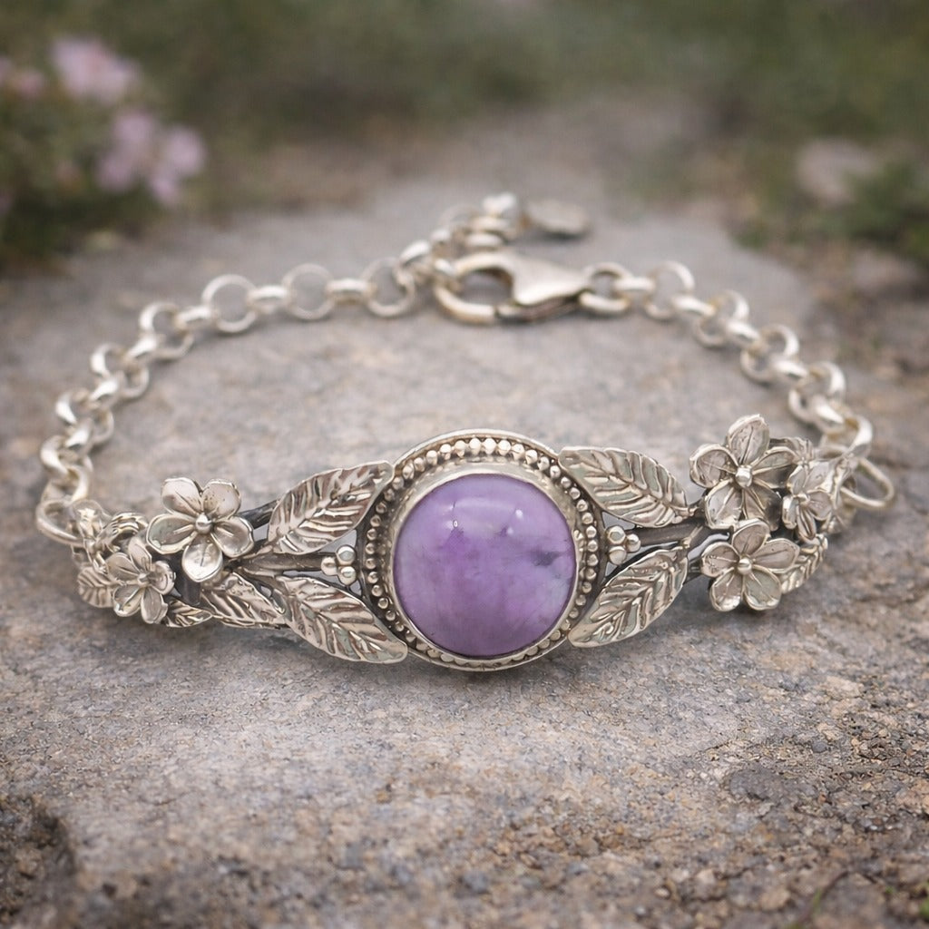 Bracciale in argento925 e ametista taglio cabochon, con piastrina rigida superiore ornata da rametti con foglie e fiori, e catenina con moschettone sul lato posteriore.