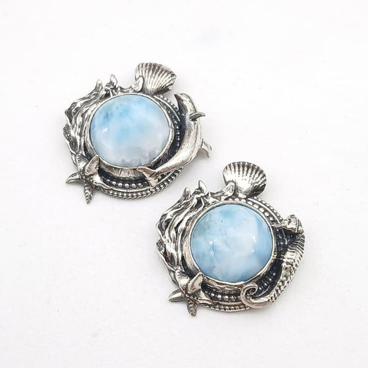 Ciondoli in argento 925 e cabochon di  larimar rotondo, circondato da decorazioni di fondale marino, alghe, conchiglie, stella marina, un cavalluccio marino per il ciondolo di destra e un delfino per quello di sinistra.