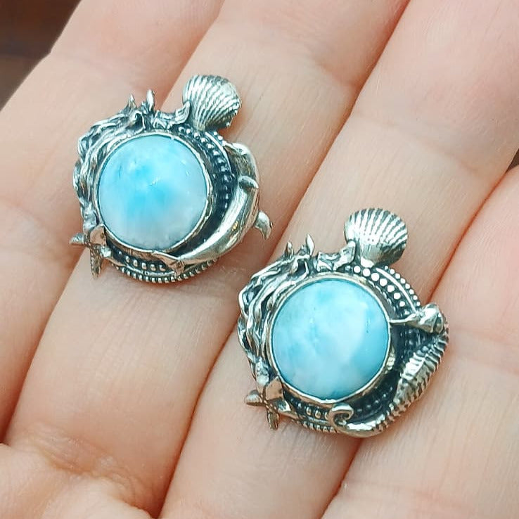 Ciondoli in argento 925 e cabochon di  larimar rotondo, circondato da decorazioni di fondale marino, alghe, conchiglie, stella marina, un cavalluccio marino per il ciondolo di destra e un delfino per quello di sinistra.
