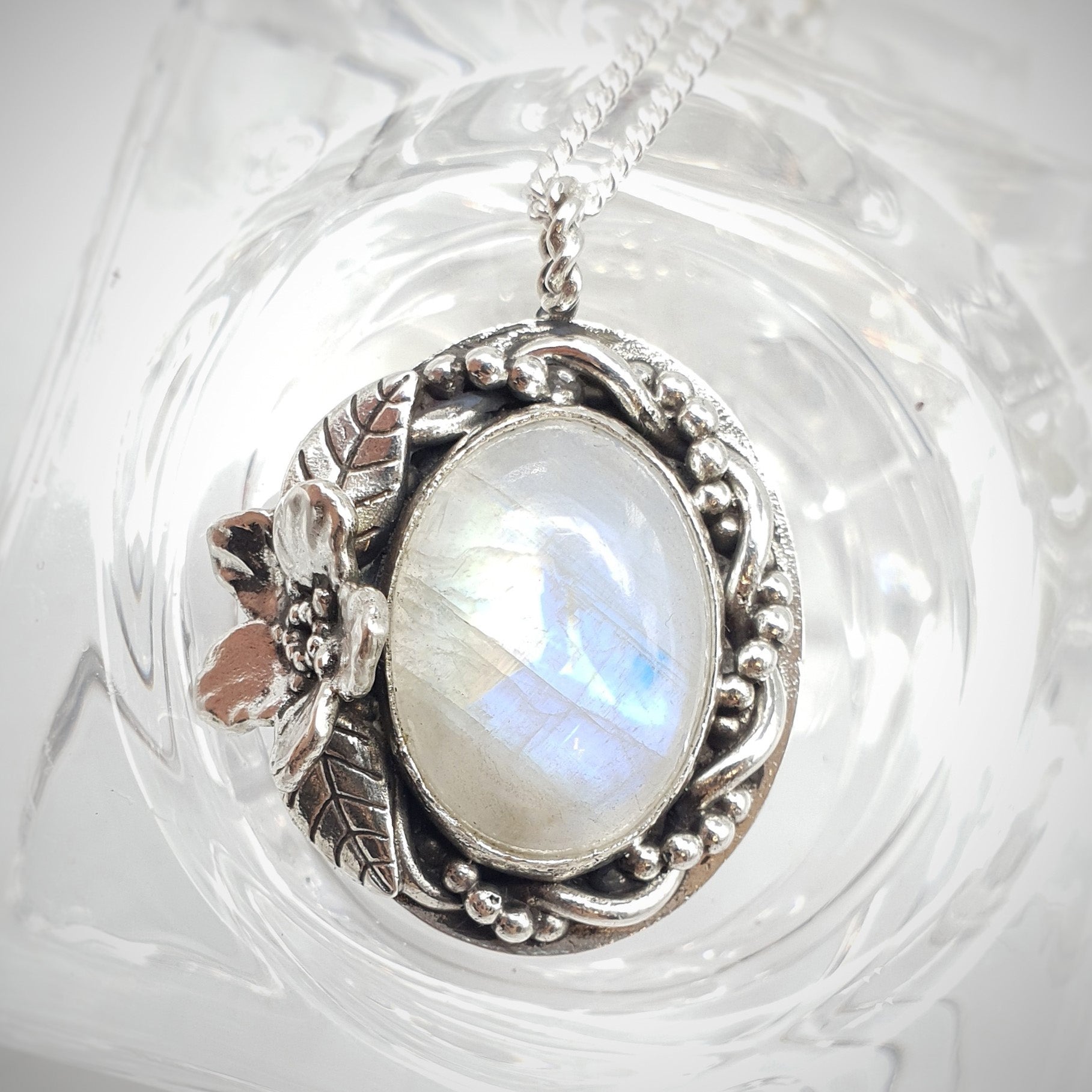 Ciondolo in argento 925 con cabochon di labradorite bianca, avvolta da un intreccio di filo e filo a palline, a sinistra un Myosotis con due foglie.