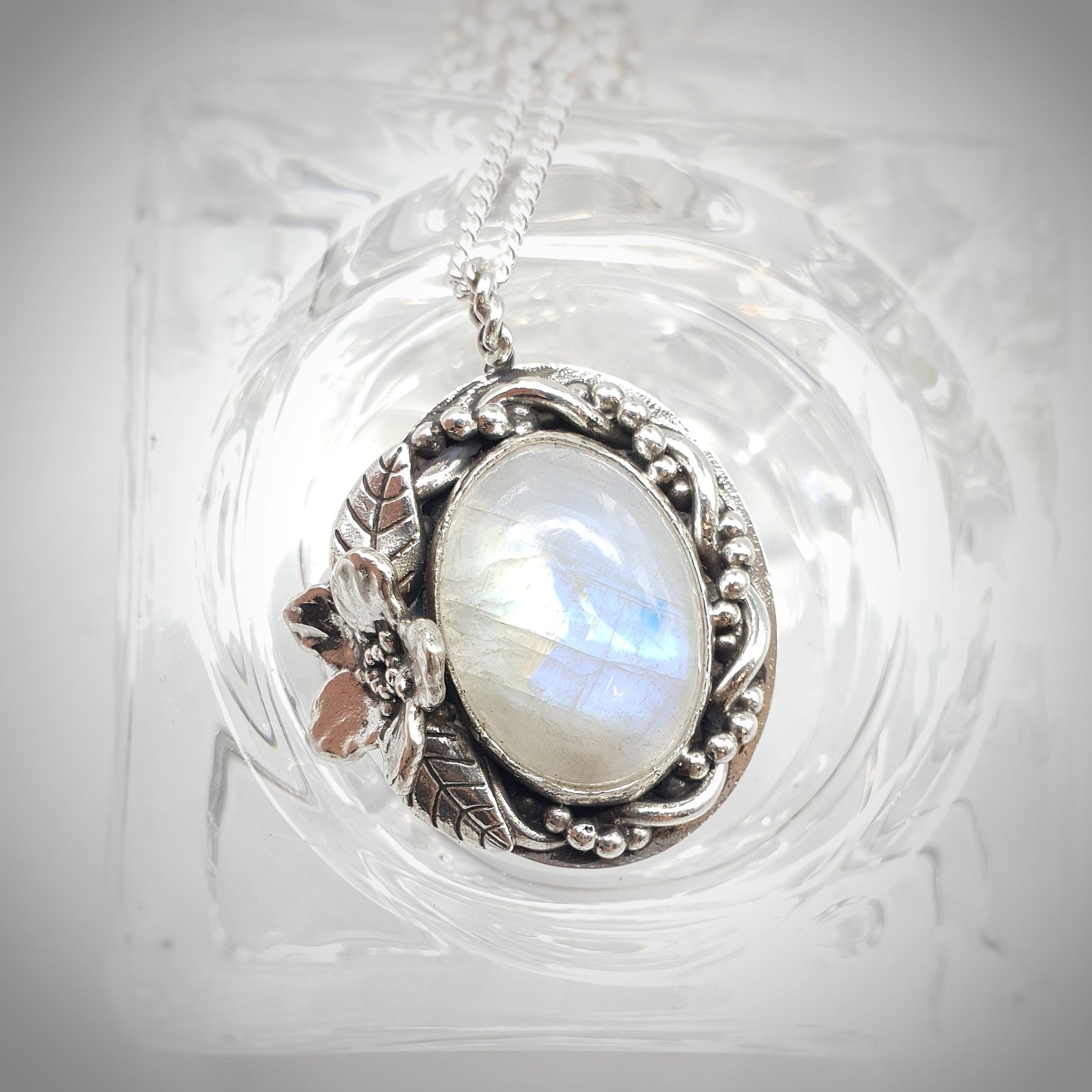 Ciondolo in argento 925 con cabochon di labradorite bianca, avvolta da un intreccio di filo e filo a palline, a sinistra un Myosotis con due foglie.