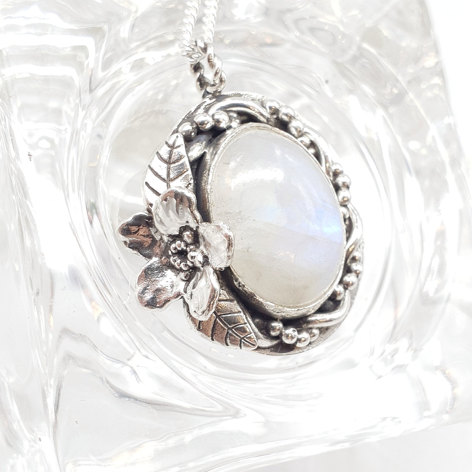 Ciondolo in argento 925 con cabochon di labradorite bianca, avvolta da un intreccio di filo e filo a palline, a sinistra un Myosotis con due foglie.