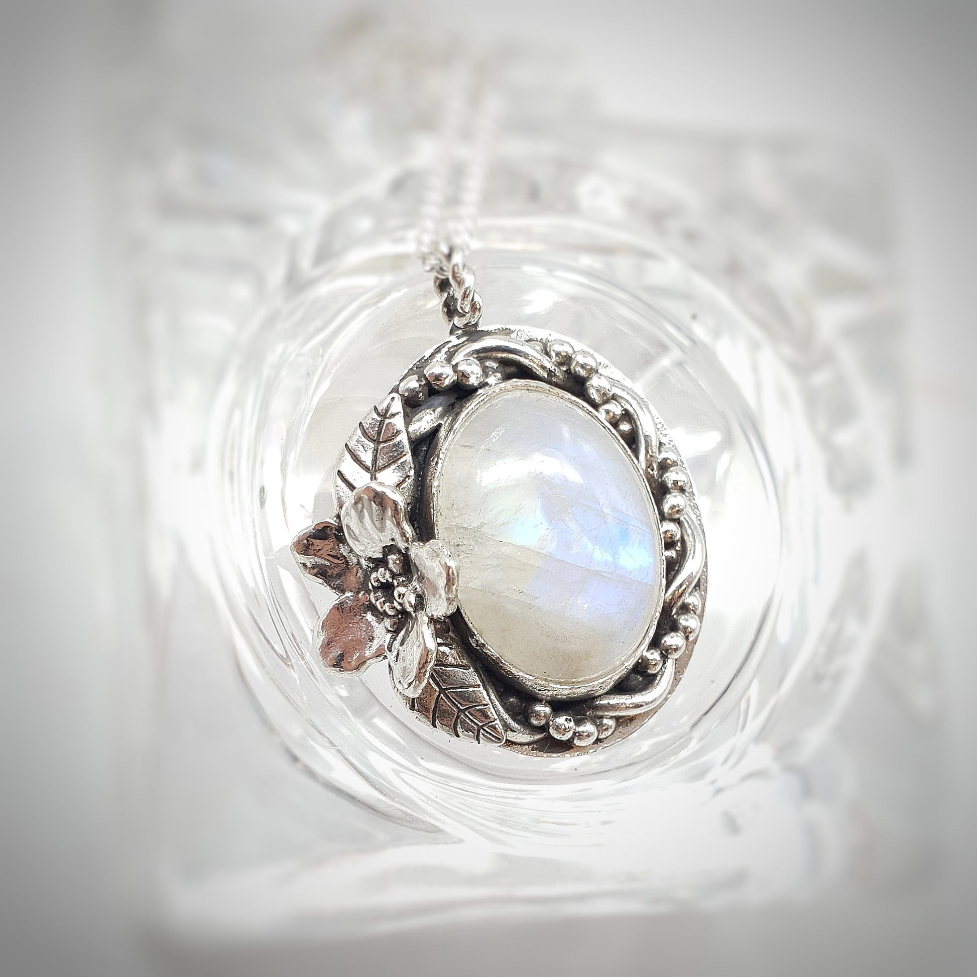 Ciondolo in argento 925 con cabochon di labradorite bianca, avvolta da un intreccio di filo e filo a palline, a sinistra un Myosotis con due foglie.