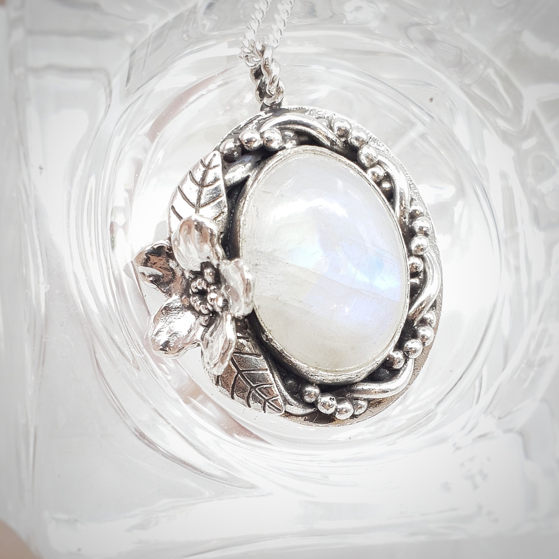 Ciondolo in argento 925 con cabochon di labradorite bianca, avvolta da un intreccio di filo e filo a palline, a sinistra un Myosotis con due foglie.