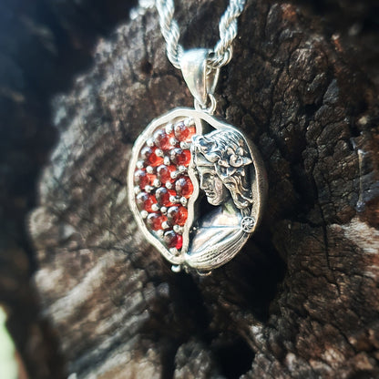 Ciondolo in argento 925 raffigurante una melagrana divisa a metà: a sinistra dodici granati rossi da 3mm, a destra una microscultura della dea Persefone.