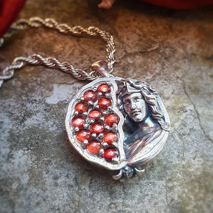 Ciondolo in argento 925 raffigurante una melagrana divisa a metà: a sinistra dodici granati rossi da 3mm, a destra una microscultura della dea Persefone.