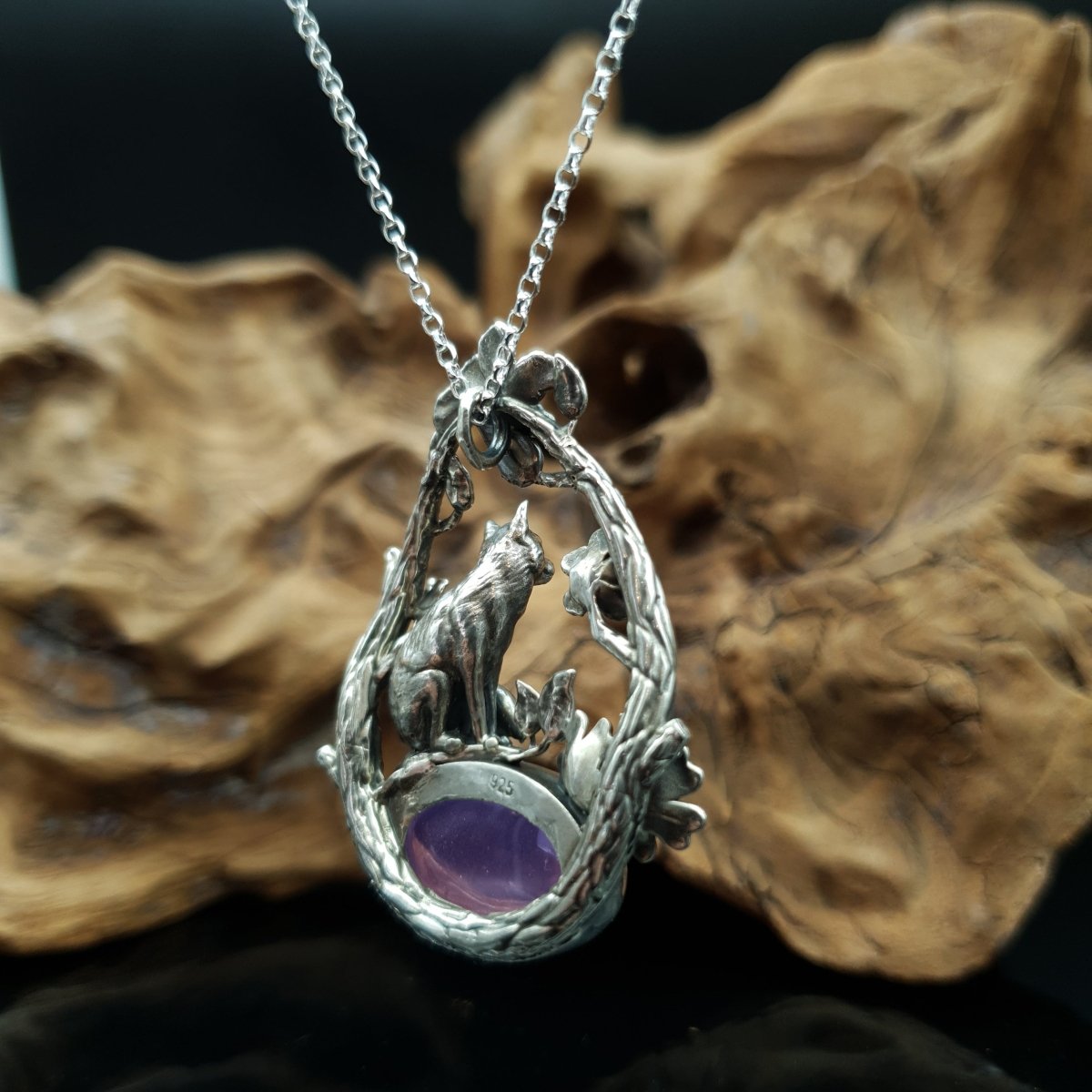 Ciondolo in argento raffigurante una volpe seduta su un cabochon ovale di ametista. La volpe è sormontata da due rami che la avvolgono, i rami sono adorni di fiori e foglie.