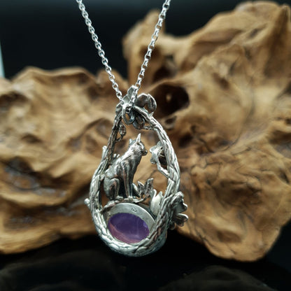 Ciondolo in argento raffigurante una volpe seduta su un cabochon ovale di ametista. La volpe è sormontata da due rami che la avvolgono, i rami sono adorni di fiori e foglie.