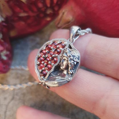 Ciondolo in argento 925 raffigurante una melagrana divisa a metà: a sinistra dodici granati rossi da 3mm, a destra una microscultura della dea Persefone.