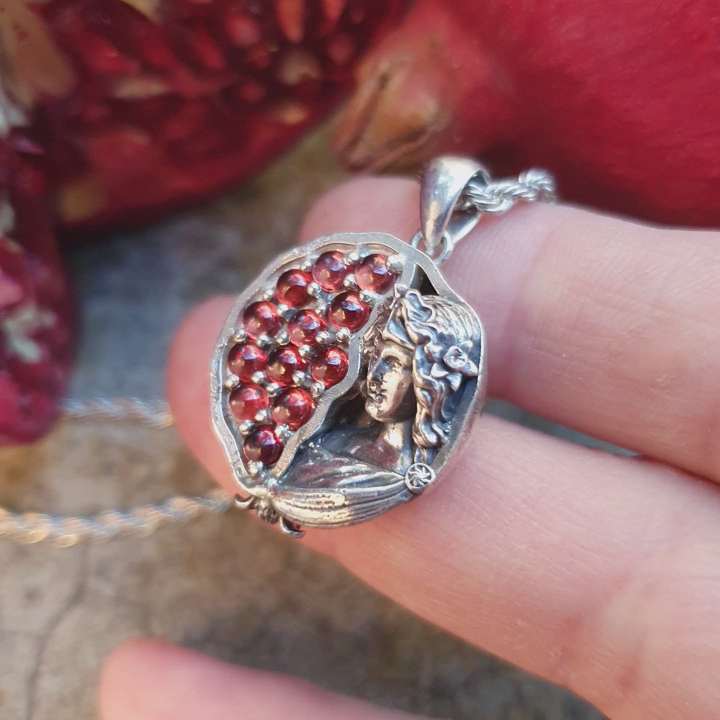 Ciondolo in argento 925 raffigurante una melagrana divisa a metà: a sinistra dodici granati rossi da 3mm, a destra una microscultura della dea Persefone.